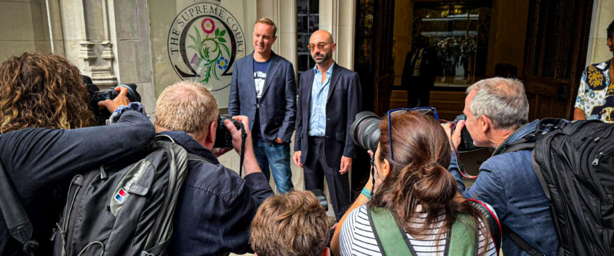 Carlo Palombo and Tom Hayes standing outside the Supreme Court, surrounded by press photographers capturing the moment their convictions were quashed.